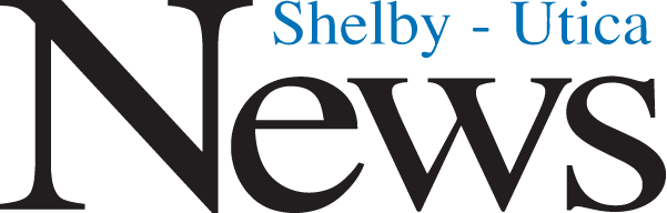 Logo for Shelby-Utica News, featuring the word 'News' in large black text and 'Shelby - Utica' in smaller blue text positioned above it. The design emphasizes the newspaper's name with a simple and clear layout.