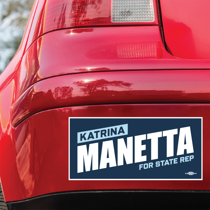 پاشەوەی ئۆتۆمبێلێکی سوور ستیکەری بەمپەرێکی هەیە کە "Katrina Manetta for State Rep" بە پیتی سپی تۆخ لەسەر پاشبنەمای شین نووسراوە.