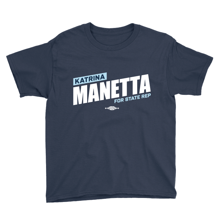 تی‌شێرتێکی شینی تاریک کە دەقی سپی و شینی کاڵی "KATRINA MANETTA FOR STATE REP" لەسەر پێشەوەکەیەتی.