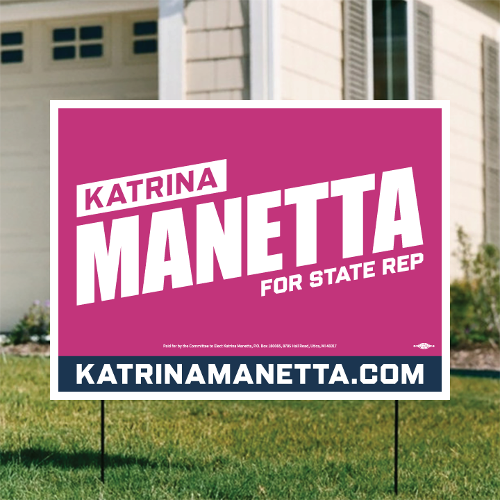 تابلۆی حەوشەیەک بە پاشبنەمای پەمەیی و دەقی سپی تۆخ کە دەڵێت "KATRINA MANETTA FOR STATE REP". لە خوارەوەی تابلۆکە ماڵپەڕی "KATRINAMANETTA.COM" نووسراوە. تابلۆکە لەبەردەم ماڵێک بە دیواری کرێمی دانراوە.